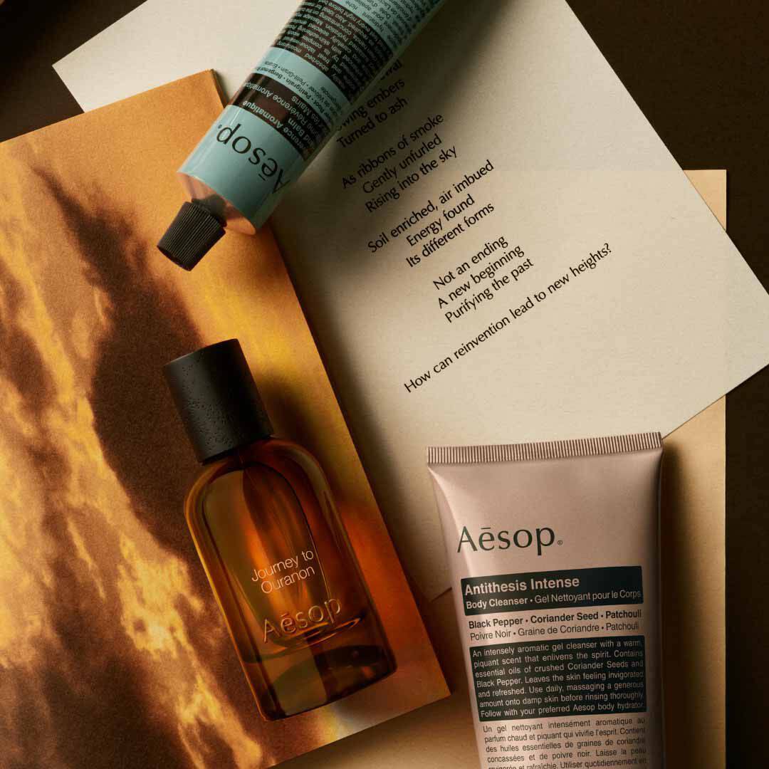 Flacon Aesop Journey to Ouranon avec flacon-pompe et tube, disposes sur des papiers avec une image de paysage lumineux.