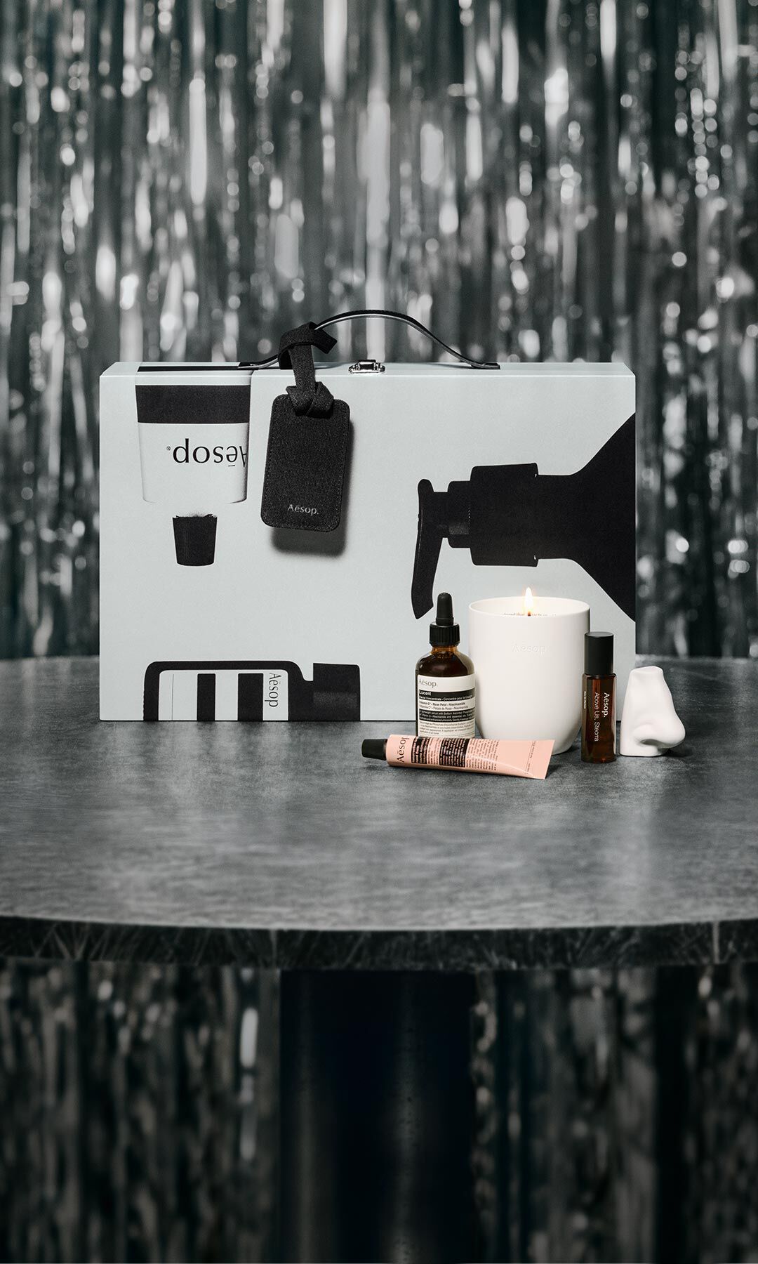 Coffret cadeau et soins Aesop disposes sur une table, devant un decor festif aux lumieres tamisees.