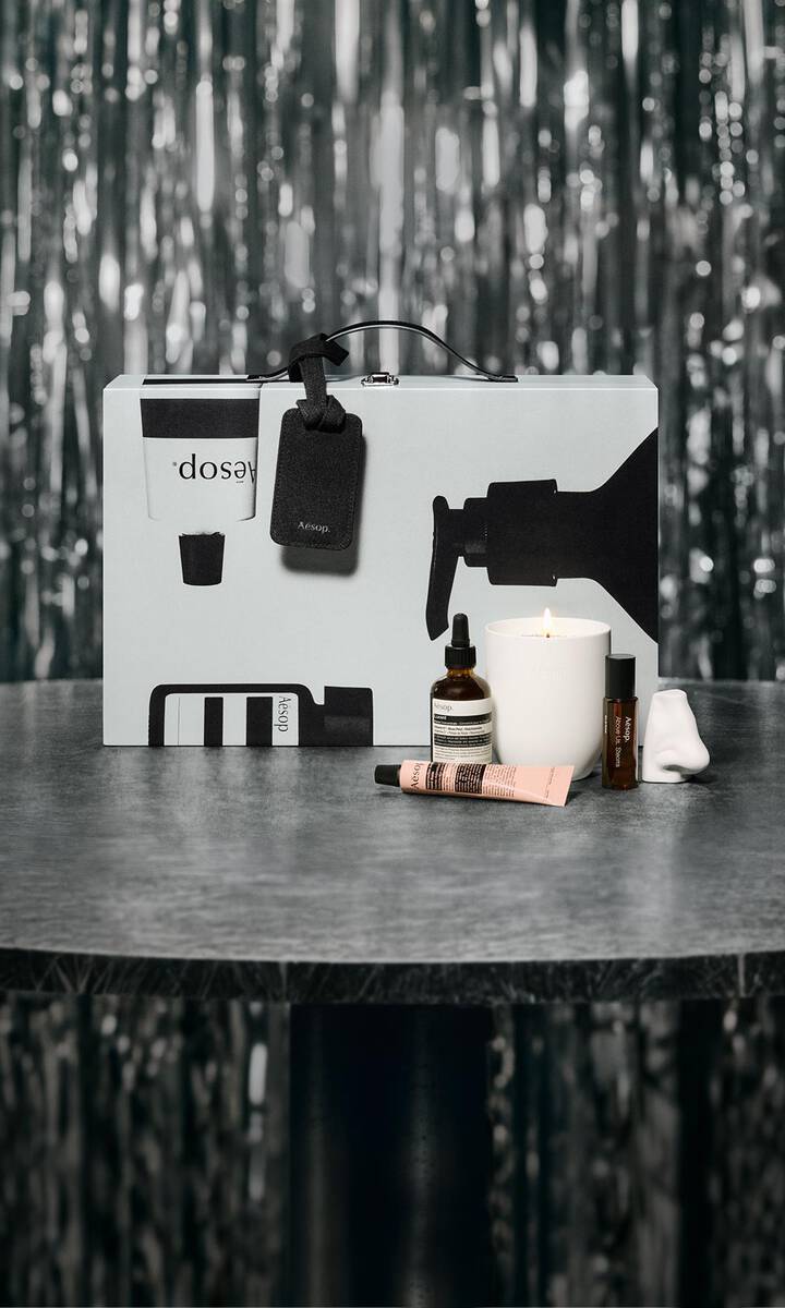 Coffret cadeau et soins Aesop disposes sur une table, devant un decor festif aux lumieres tamisees.