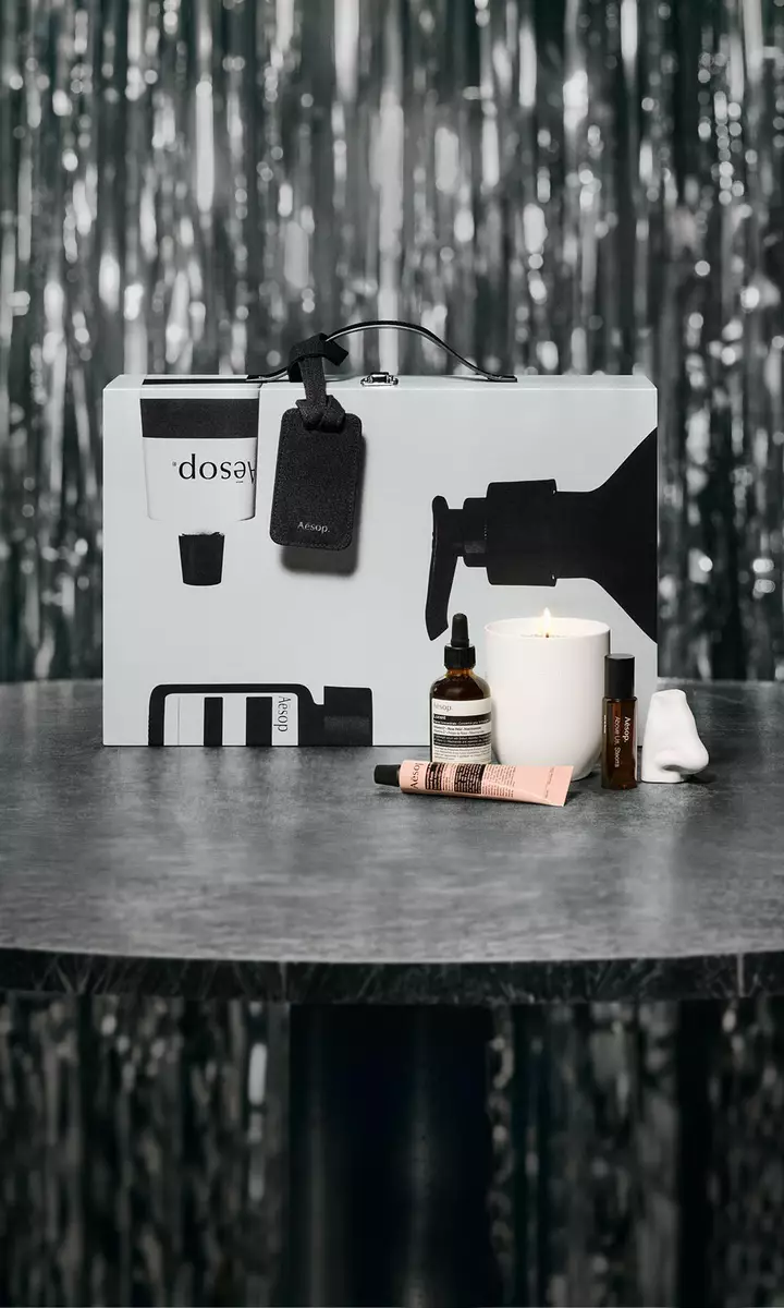 Coffret cadeau et soins Aesop disposes sur une table, devant un decor festif aux lumieres tamisees.