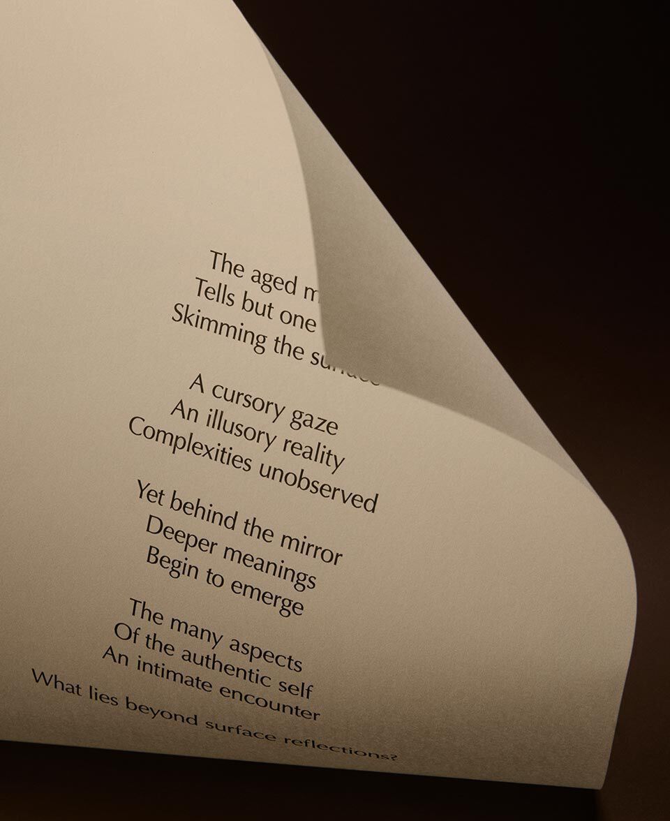 Papier creme plie, imprime de vers, dans un decor sombre et minimaliste.