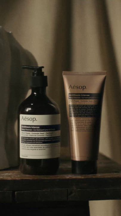Aesop Antithesis Intense Body Cleanser pump bottle and tube beside a white torso sculpture on a wooden work table.