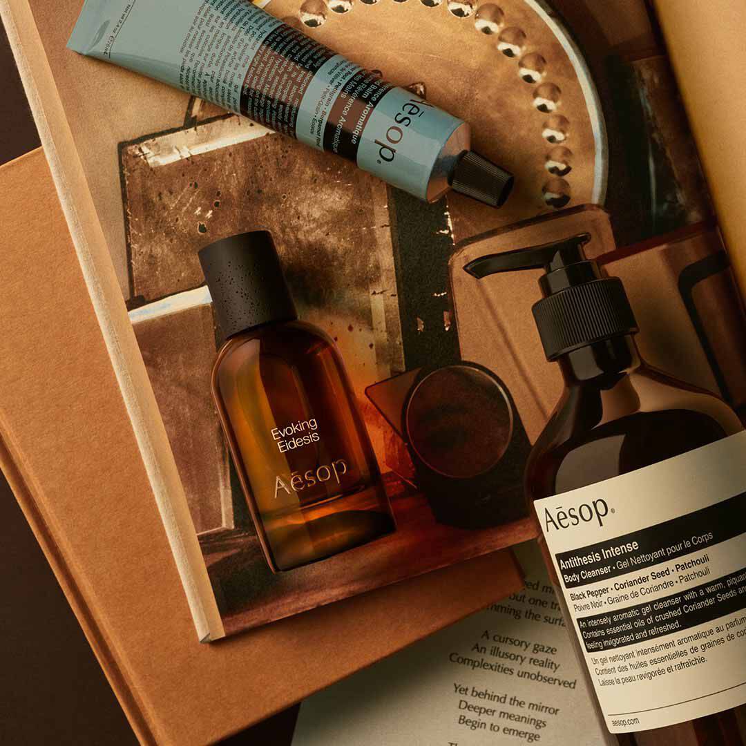 Flacon Aesop Evoking Eidesis avec flacon-pompe et tube bleu, disposes sur des papiers et des visuels de plateau miroir.