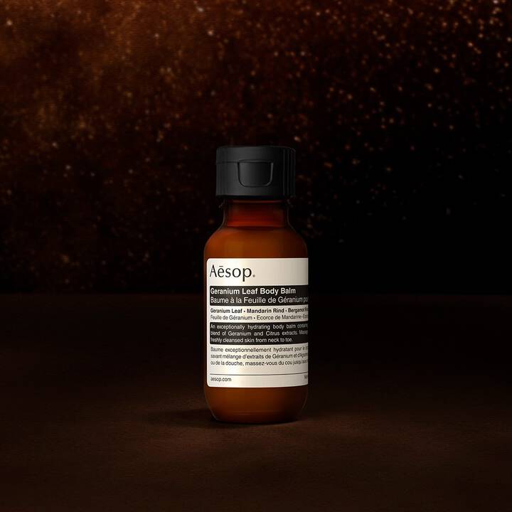 Un flacon de baume pour le corps Geranium Leaf d'Aesop sur un fond sombre et texture.