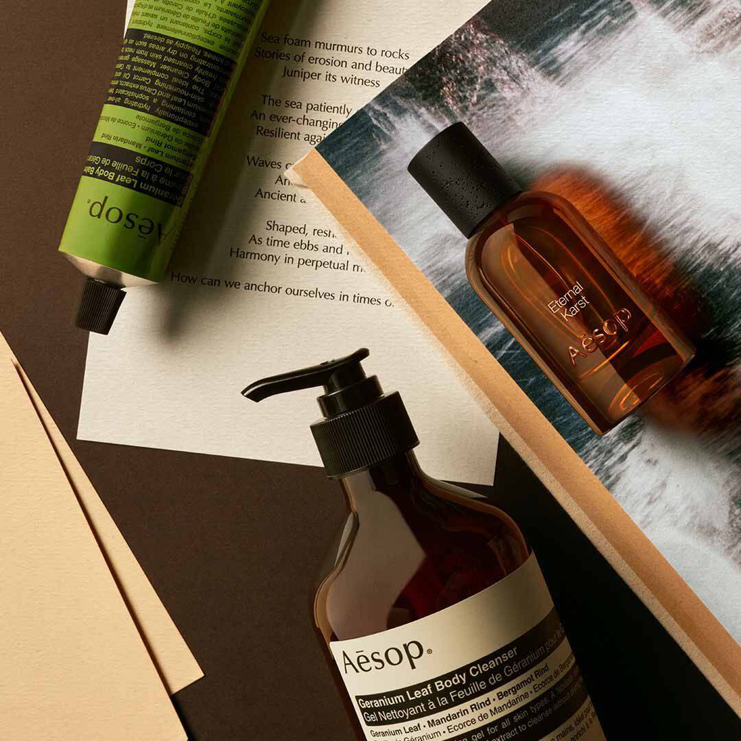 Flacon Aesop Eternal Karst avec flacon-pompe et tube vert, disposes sur des papiers avec des visuels d’eau ecumante.
