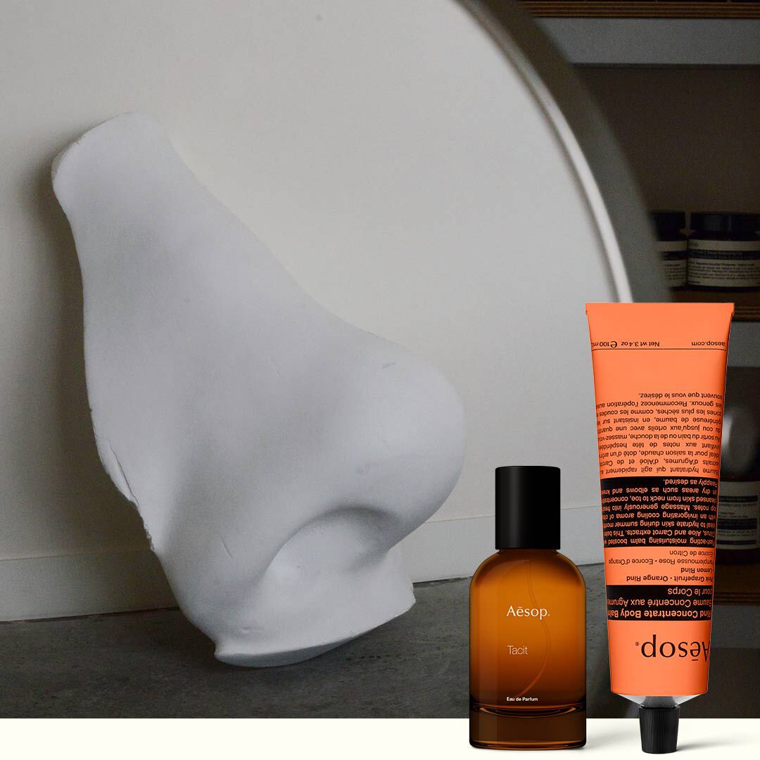 Flacon de parfum ambre et creme pour les mains corail a cote d’une sculpture blanche