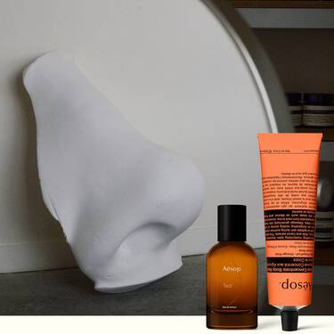 Flacon de parfum ambre et creme pour les mains corail a cote d’une sculpture blanche