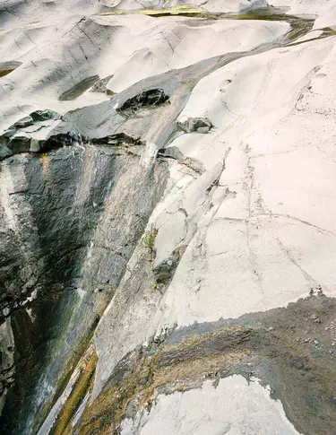Surface minerale de pierre claire, marbree de stries blanches, grises et anthracite, aux textures superposees, traversee d’une fissure diagonale.