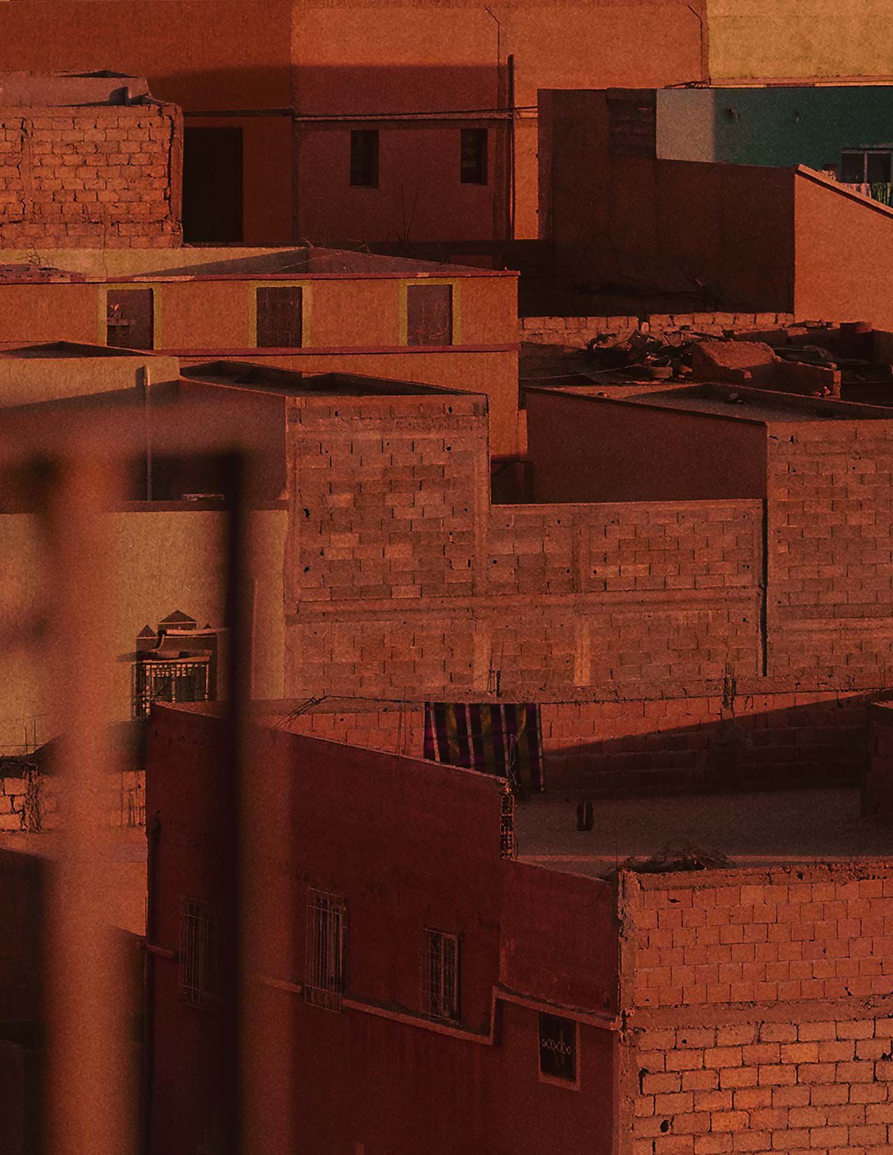 Toits et murs d’une ville de terre cuite baignes d’une chaude lumiere rouge rouille, avec une architecture massive, des facades ombragees et des surfaces de maconnerie texturees.