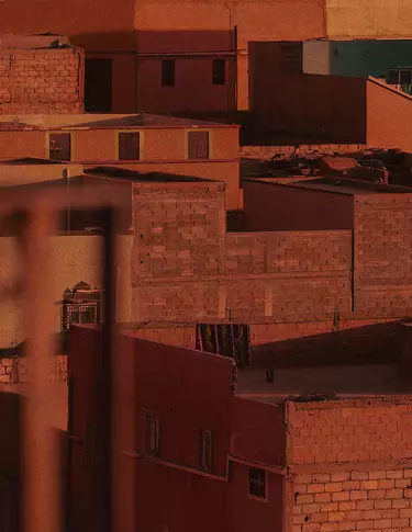 Toits et murs d’une ville de terre cuite baignes d’une chaude lumiere rouge rouille, avec une architecture massive, des facades ombragees et des surfaces de maconnerie texturees.