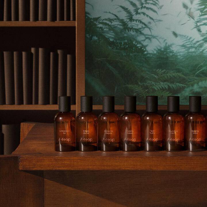 Une rangee de flacons de parfum en verre ambre Aesop sur une etagere en bois.