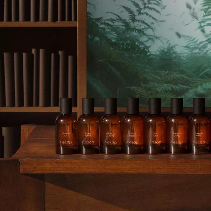 Une rangee de flacons de parfum en verre ambre Aesop sur une etagere en bois.