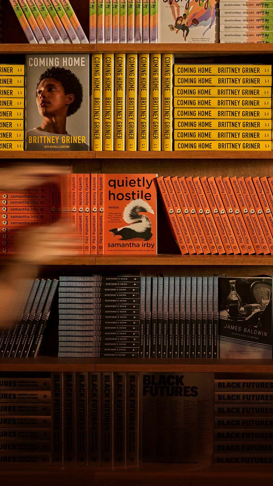 Blurred person walking past warm wooden shelves filled with yellow, orange, and red books.