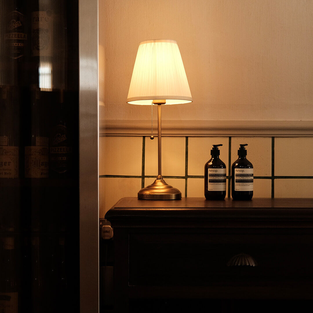 Deux flacons Aesop sur une table d'entree, accompagnes d'une lampe antique.