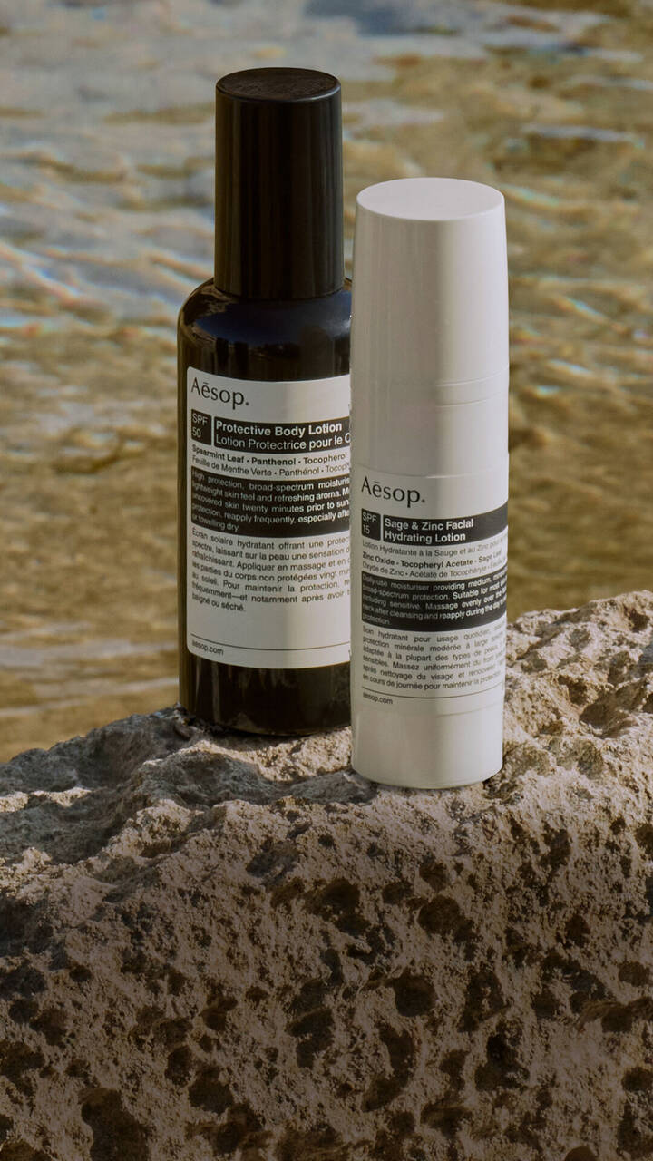 Une selection soignee de formulations de protection solaire Aesop reposant sur une roche au bord de la mer.