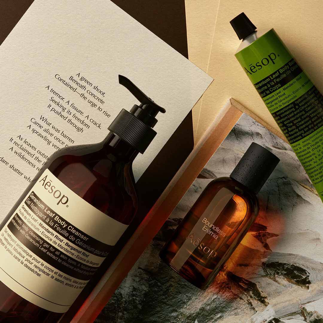 Flacon Aesop Boundless Eremia avec flacon-pompe et tube vert, disposes sur des papiers et une image de pierre.